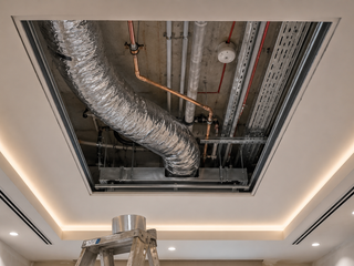 Service access panel open showing tidy AC ducts, condensate drain and electrical above the ceiling