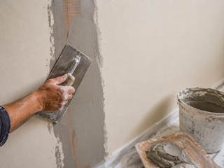 Mesh-reinforced plaster crack repair on a villa wall with fibreglass mesh in fresh patch