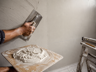 Plasterer's hands smoothing a fresh skim coat with a stainless trowel across a villa wall